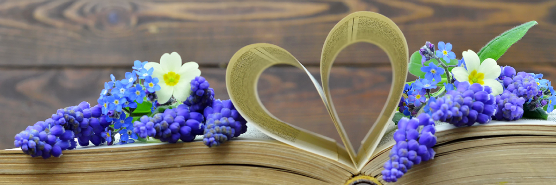Decorative flowers on top of a book with pages folded into a heart shape. 