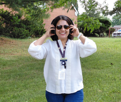 Nazia, PSA, walking in a park, touching her headphones and smiling. 